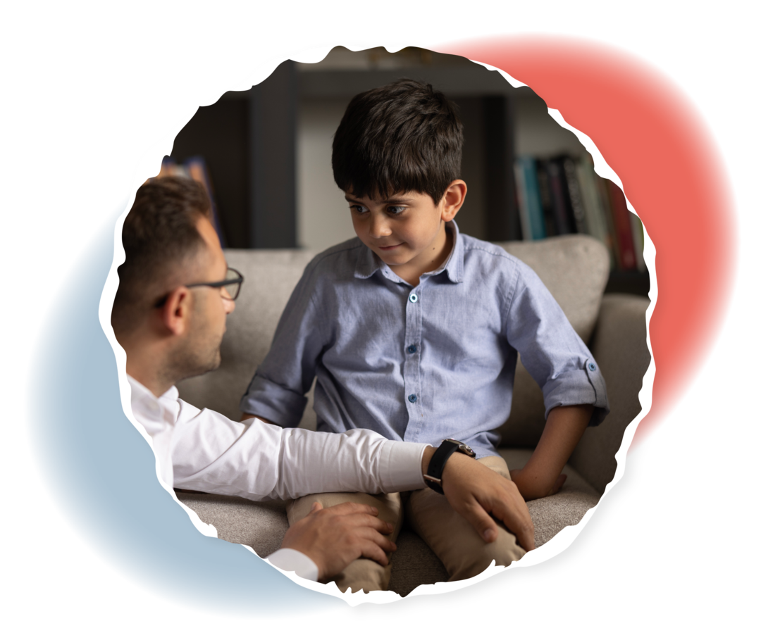 Ein Mann kniet neben einem Jungen, der auf einem Sofa sitzt.