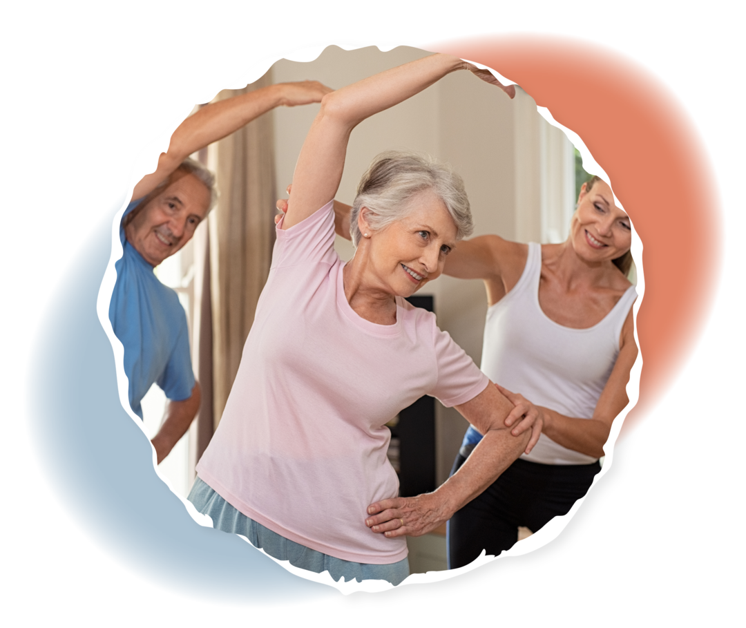 Eine Frau und ein Mann im Seniorenalter werden von einer Trainerin bei gymnastischen Übungen unterstützt. 