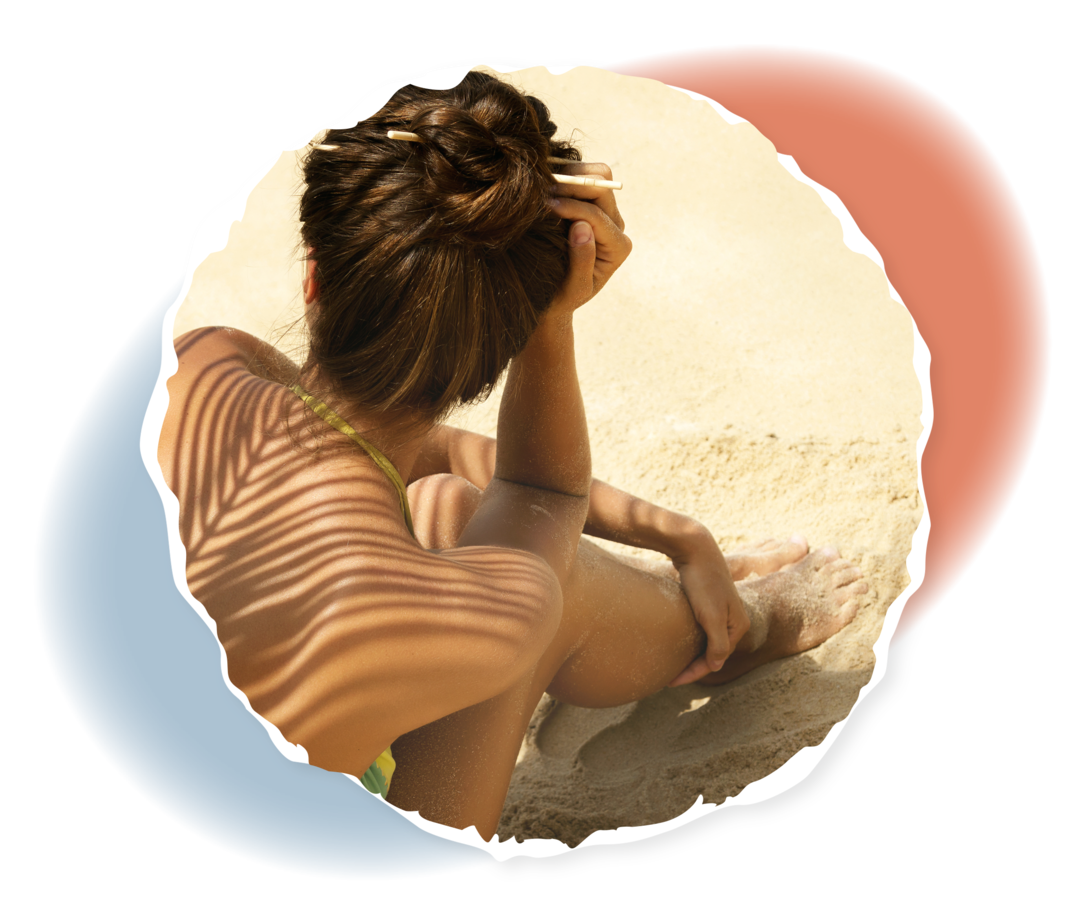 Eine Person sitzt im Sand, auf ihrem Rücken ist der Schatten eines Palmenwedels zu sehen. 