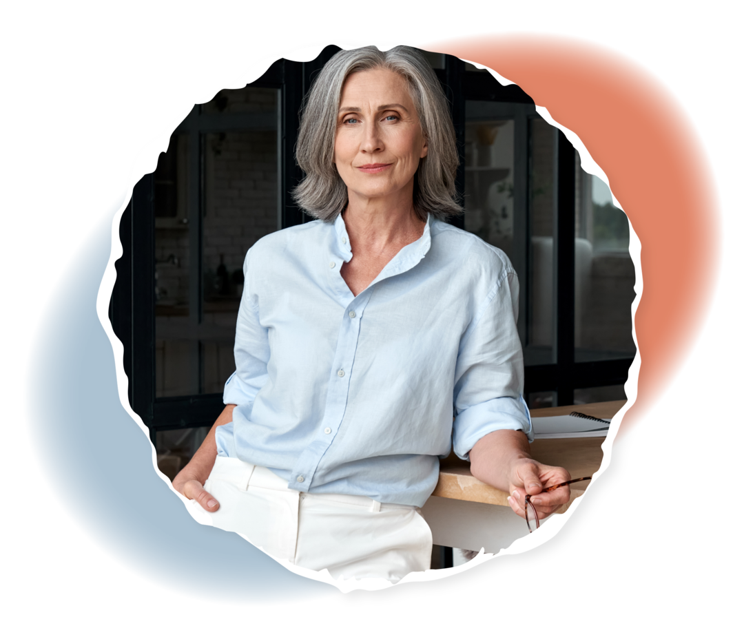 Eine ältere Person lehnt an einem Tisch und blickt in die Kamera. 