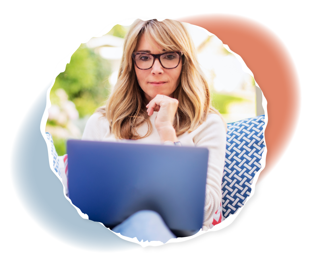 Eine ältere Person sitzt auf einer Sitzgelegenheit und betrachtet den Laptop auf ihrem Schoß.  