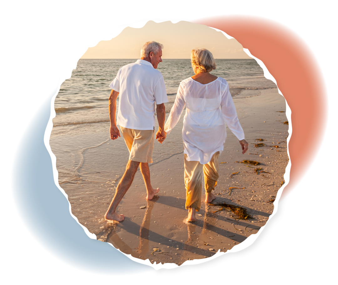 Ein älteres Paar geht im Sonnenuntergang Hand in Hand am Strand spazieren.