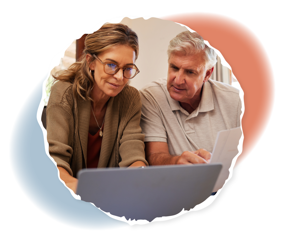 Ein Mann und eine Frau schauen auf einen Laptop. Der Mann hält einige Unterlagen in seiner Hand. 