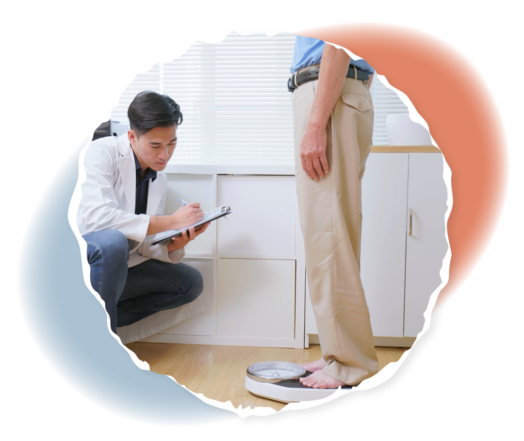 Eine Person steht auf einer Waage, neben ihr kniet eine andere Person in weißem Kittel, die sich etwas auf einem Klemmbrett notiert. 