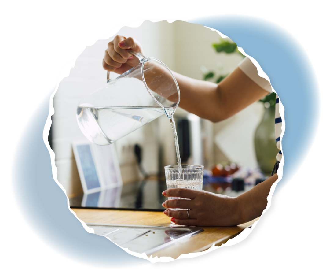 Eine Person gießt Wasser aus einer Karaffe in ein Glas. 