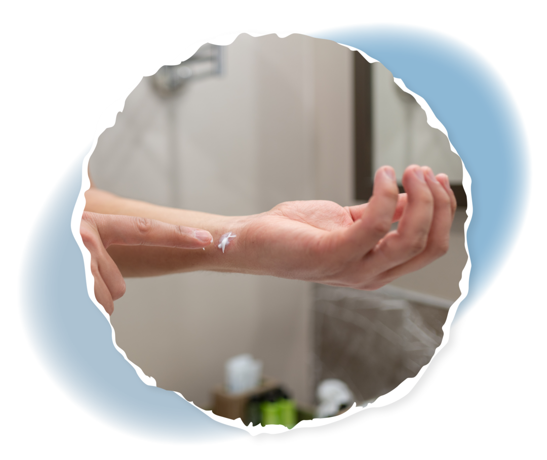 Eine Person steht im Badezimmer und cremt eine Stelle am linken Handgelenk ein. 