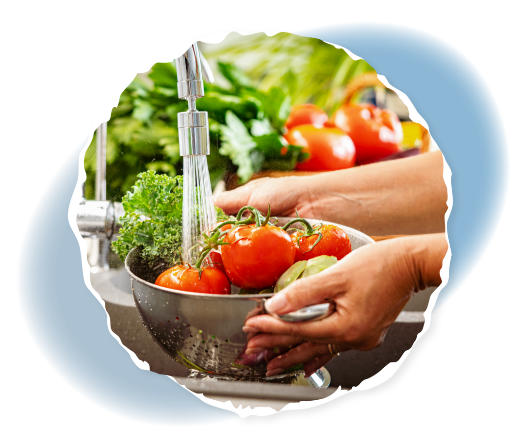 Hygienemaßnahmen nach Stammzelltransplantation Eine Person wäscht verschiedenes Gemüse in einem Sieb unter einem Wasserhahn.